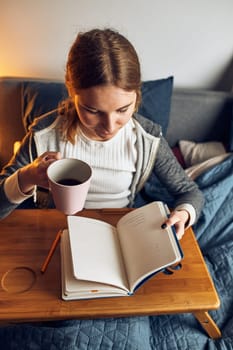 Student learning at home. Young woman making notes, reading and learning from notepad. Girl writing journal sitting in bed at home during quarantine