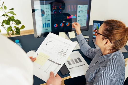 Woman entrepreneur discussing financial data with her colleague sitting at desk in office. Happy positive businesswoman working with charts and tables on computer. Two people working together. Workmates talking about project