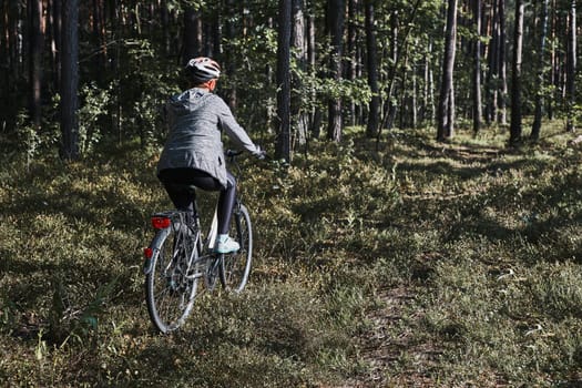 Active woman cycling on forest road. Female riding bicycle off-road route on summer vacation day. Woman wearing bicycle helmet and gloves