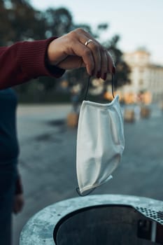 Woman female hand throwing out used face mask to trash