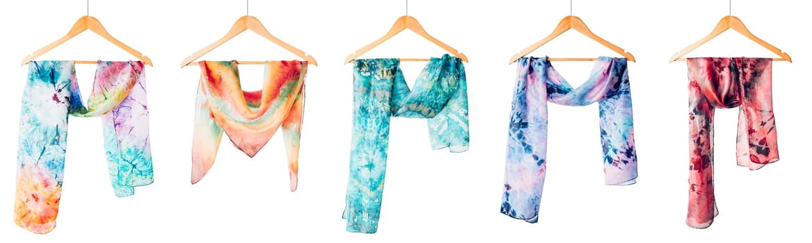 Silk colourful hand painted tied scarves hung on hangers over white background. Woman fashion, tying a scarf, wearing a scarves. Stylish ways to tie and wear scarves