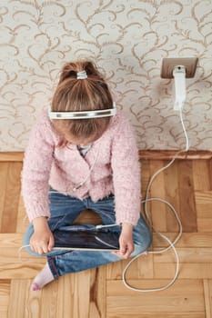Little girl preschooler learning online solving puzzles playing educational games listetning to music and sounds using tablet and headpphones at home during pandemic quarantine
