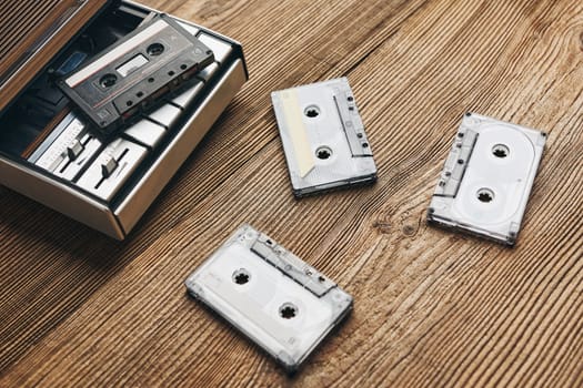Compact cassette tapes and cassette recorder on wooden table. Retro music style. 80s music party. Vintage style. Analog equipment. Stereo sound. Back to the past