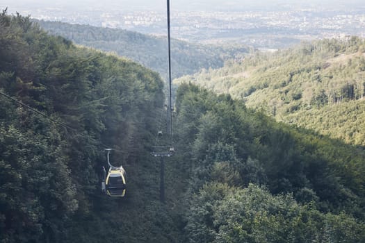 Cable car go to top of mountain among trees in forest on summer sunny day. Panoramic view of valley at mountain