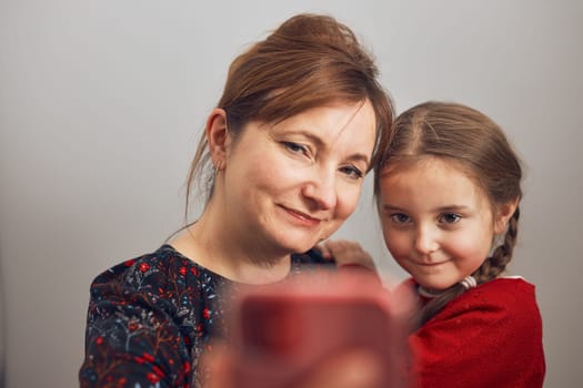 Mother with her little daughter making video call using mobile phone. Keeping distance. Woman and little girl talking with relatives. Cheerful family having fun taking selfie photo using smartphone. Connecting remotely with family