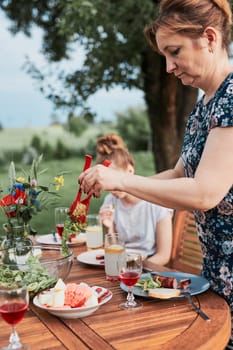 Woman having a meal from grill during summer family picnic outdoor dinner in a home garden. Close up of people sitting at a table with food and dishes