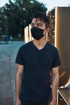 Young man standing in the city center in the evening looking away wearing the face mask to avoid virus infection and to prevent the spread of disease in time of coronavirus