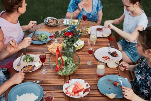 Family having a meal from grill during summer picnic outdoor dinner in a home garden. Close up of people sitting at a table with food and dishes