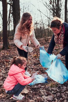 Family cleaning up a forest. Volunteers picking plastic waste to bags. Concept of plastic pollution and too many plastic waste. Environmental issue. Environmental damage. Responsibilitiy for environment. Real people, authentic situations