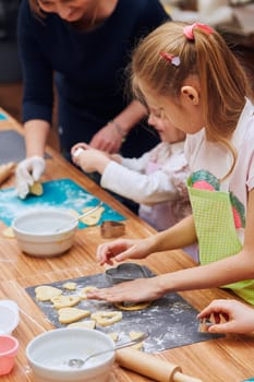 Girls cutting the dough to heart shapes for the cookies. Kids taking part in baking workshop. Baking classes for children, aspiring little chefs. Girls learning to cook. Combining and stirring prepared ingredients. Real people, authentic situations