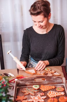 Woman decorating baked Christmas gingerbread cookies with frosting