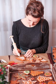 Woman decorating baked Christmas gingerbread cookies with frosting