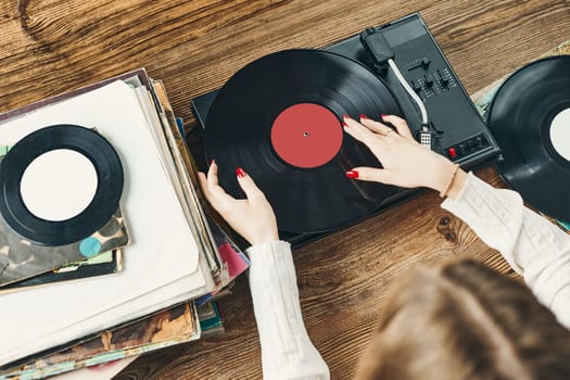 Young woman listening to music from vinyl record player. Playing music on turntable player. Female enjoying music from old record collection at home. Stack of analog vinyl records. Retro and vintage music style. Music Passion and hobby