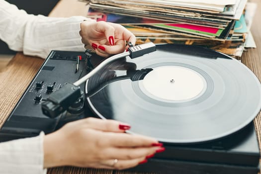 Young woman listening to music from vinyl record player. Playing music on turntable player. Female enjoying music from old record collection at home. Stack of analog vinyl records. Retro and vintage music style. Music Passion and hobby