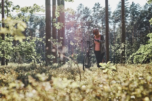 Active woman cycling on forest road. Female riding bicycle off-road route on summer vacation day. Woman wearing bicycle helmet and gloves