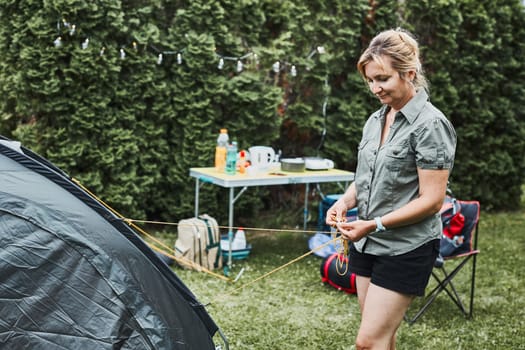Woman putting up a tent at camping during summer vacation. Female preparing campsite to rest and relax. Spending vacations outdoors close to nature