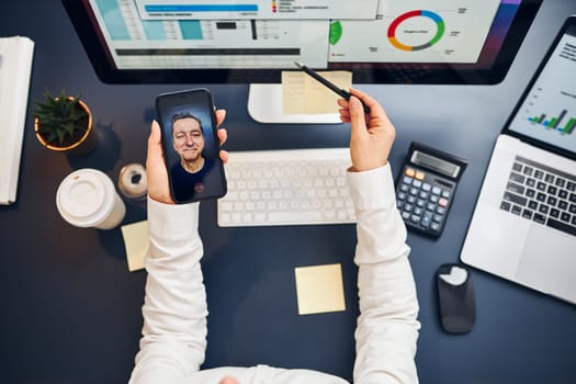 Businesswoman having video chat on smartphone with her client. Businesswoman working with data on charts, graphs and diagrams on computer screen. Woman holding smartphone sitting at desk in office