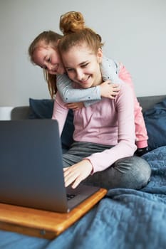 Grandchildren teenage girl and her younger sister talking on video call with granparents on laptop from home during COVID-19 quarantine. Girls sitting on bed in front of computer