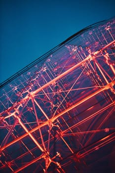 Looking up at modern glass building lighted with red at night. View from bottom up the deep blue sky