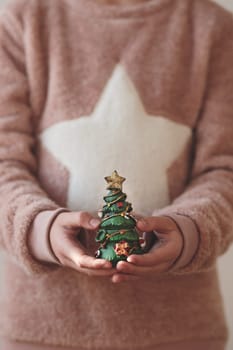 Girl wearing warm sweater holding Christmas tree figurine