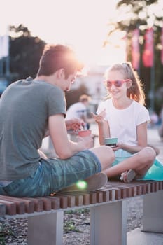 Girl and boy spending time together in the city centre eating ice cream on a summer day