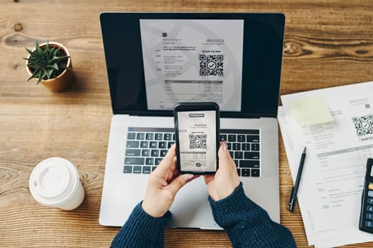 Woman scanning QR code from invoice to make payment using fast secure payment system and smartphone code reader. Business woman paying bills using express payment technology. Female using mobile phone and laptop. Paying expenses online