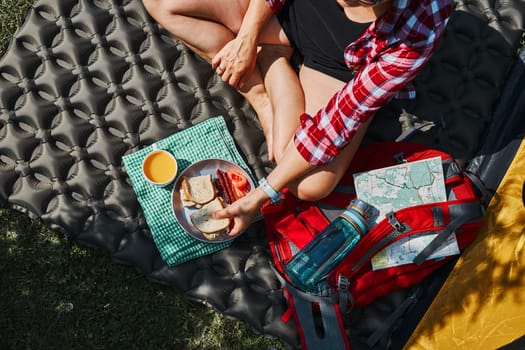 Woman having breakfast sitting by tent at camping. Female actively spending summer vacations close to nature outdoors. Concept of camp life