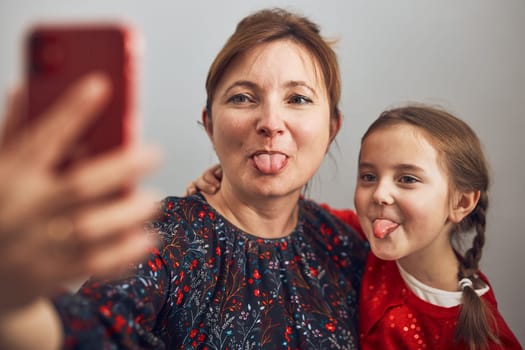 Mother with her little daughter making video call using mobile phone. Keeping distance. Woman and little girl talking with relatives. Cheerful family having fun taking selfie photo using smartphone. Connecting remotely with family