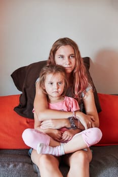 Teenage girl and her little sister watching TV together, sitting concentrated on sofa at home. Real people, authentic situations