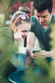 Couple of friends, teenage girl and boy,  having fun with smartphones, sitting in center of town, spending time together