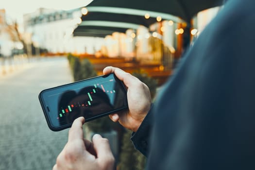 Person investing trading on stock cryptocurrency market using investing application on smartphone. Stock market investment in hand. Trader holding mobile phone looking at candle chart