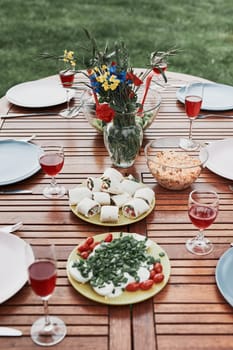 Dinner in an apple orchard garden on wooden table with salads and wine decorated with flowers. Close up of table with food prepared for family dinner
