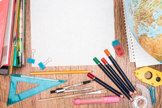 School accessories, pencil, pen, scissors, blank sheet of paper on a wooden desk. View from above