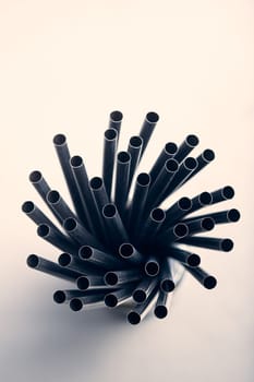 Bunch of black plastic straws scattered in container over plain grey background. Copy space for text