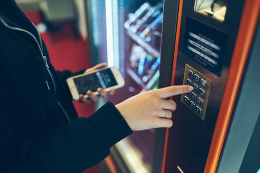 Woman paying for product at vending machine using contactless method of payment with mobile phone. Woman using new way of payments