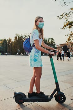 Young woman riding an electric scooter in the city center. Woman wearing the face mask to avoid virus infection and to prevent the spread of disease in time of coronavirus. Candid people, real moments, authentic situations