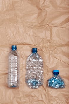 Squashed empty plastic bottles put in a row, over crumpled brown paper background. Collecting plastic waste to recycling. Concept of plastic pollution and too many plastic waste. Copy space for text