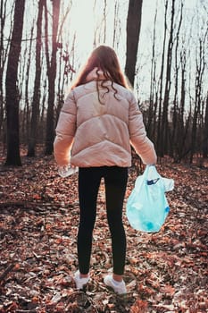Young woman cleaning up a forest. Volunteer picking plastic waste to bags. Concept of plastic pollution and too many plastic waste. Environmental issue. Environmental damage. Responsibilitiy for environment. Real people, authentic situations