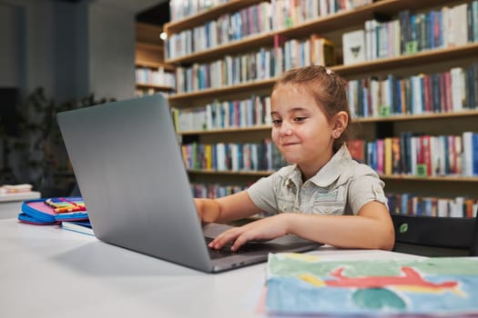 Pleased little student having video class remotely with her teacher on laptop sitting at desk in after school club at primary school. Back to school. Child using technology on elementary computer science lesson. Smart little girl learning online. Teacher teaching remotely. E-learning classes