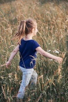 Little happy girl walking through a tall grass in the countryside. Candid people, real moments, authentic situations