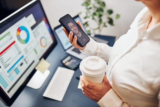 Businesswoman having video chat on mobile phone with her colleague. Businesswoman working with data on charts, graphs and diagrams on computer screen. Woman holding smartphone sitting at desk in office