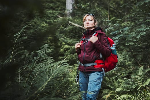 Woman with backpack hiking in forest, actively spending summer vacation close to nature. Woman walking on path among trees