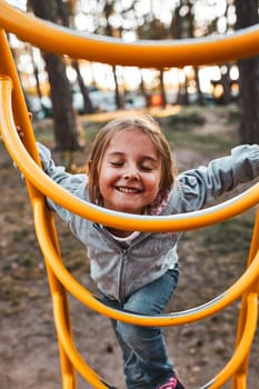 Playful happy girl preschooler playing on a playground climbing on monkey bars smiling with closed eyes. Child having fun playing outdoors in a park on summer day