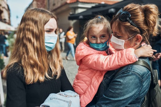 Family mother and her daughters standing in a street downtown wearing the face masks to avoid virus infection and to prevent the spread of disease in time of coronavirus