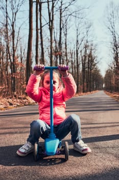 Little girl playing in the park, riding a scooter, having fun on sunny autumn day. Real people, authentic situations