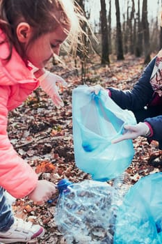 Family cleaning up a forest. Volunteers picking plastic waste to bags. Concept of plastic pollution and too many plastic waste. Environmental issue. Environmental damage. Responsibilitiy for environment. Real people, authentic situations