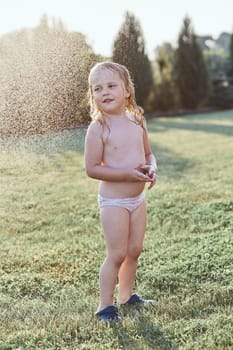 Little cute adorable girl enjoying a cool water sprayed by her mother during hot summer day in backyard. Candid people, real moments, authentic situations