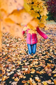 Girl jumping behind yellow autumn leaves in a park