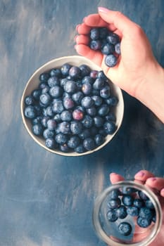 Woman putting freshly gathered blueberries from a jar into a small bowl. Table painted in blue in the background