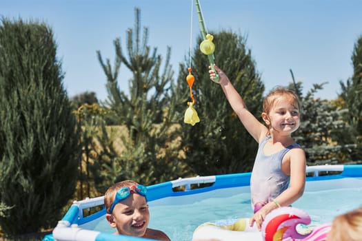 Children playing in a pool with fishing rod toy in a home garden. Kids having fun playing together on a summer sunny day